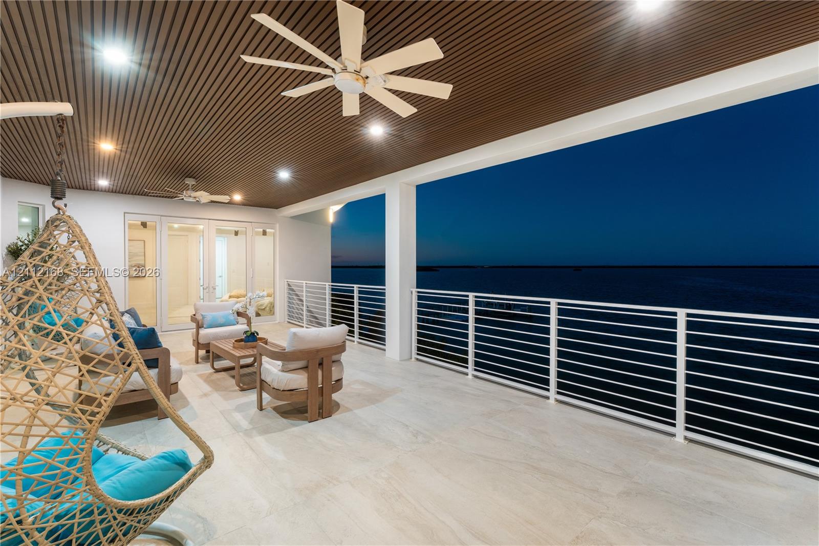 Covered terrace featuring a slatted wood-finish ceiling, large-format tile flooring, white metal horizontal railing, and recessed lighting