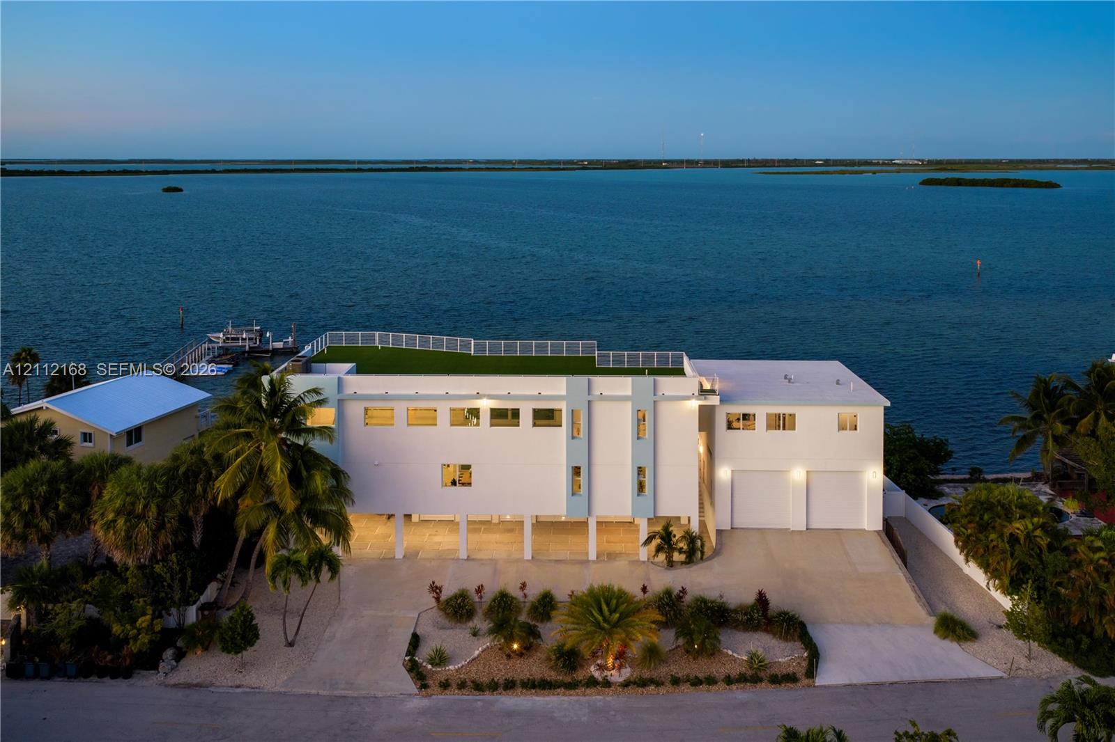 Waterfront estate featuring a rooftop terrace, elevated structural design, integrated two-car garage, private dock, and mature palm landscaping