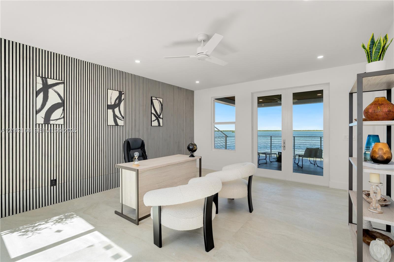 Accent wall with vertical paneling, light-toned flooring, white ceiling fan, and double glass doors providing external water-front access