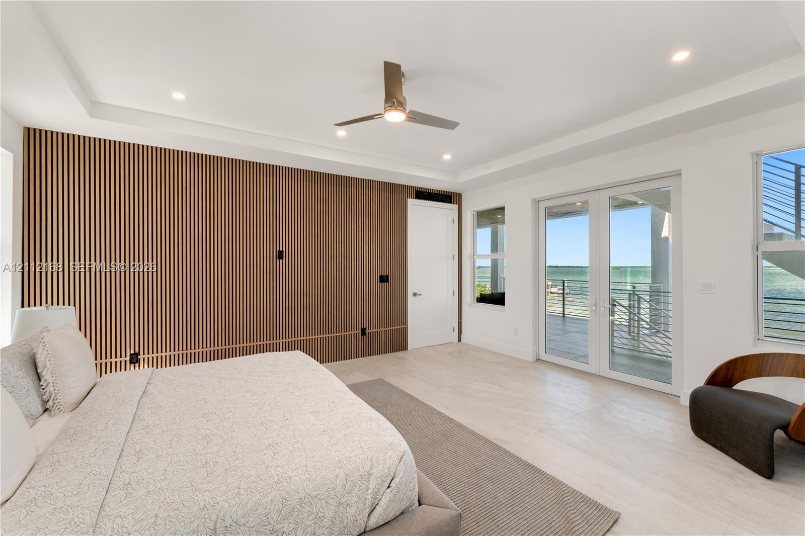 Slatted wood-finish accent wall, tray ceiling with recessed lighting, light-toned wood-finish flooring, and glass French doors leading to an exterior balcony