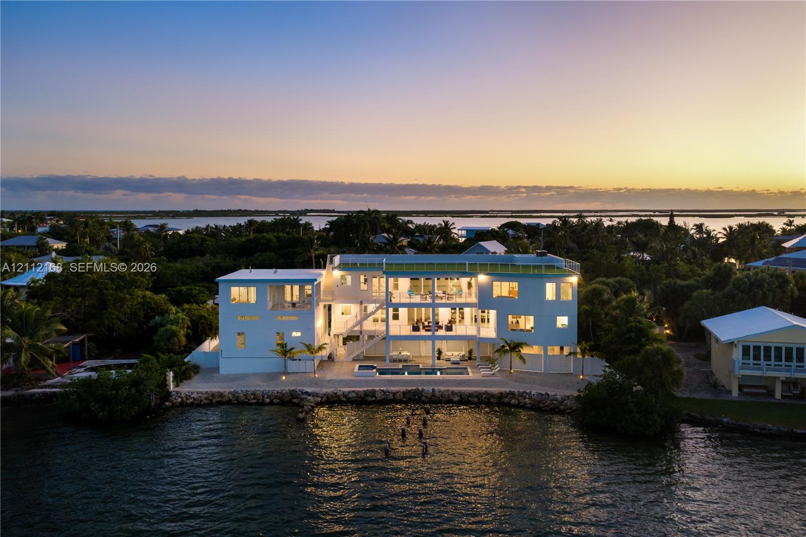 Waterfront residence featuring multi-level balconies, an in-ground swimming pool, a rock-lined shoreline, and a rooftop terrace