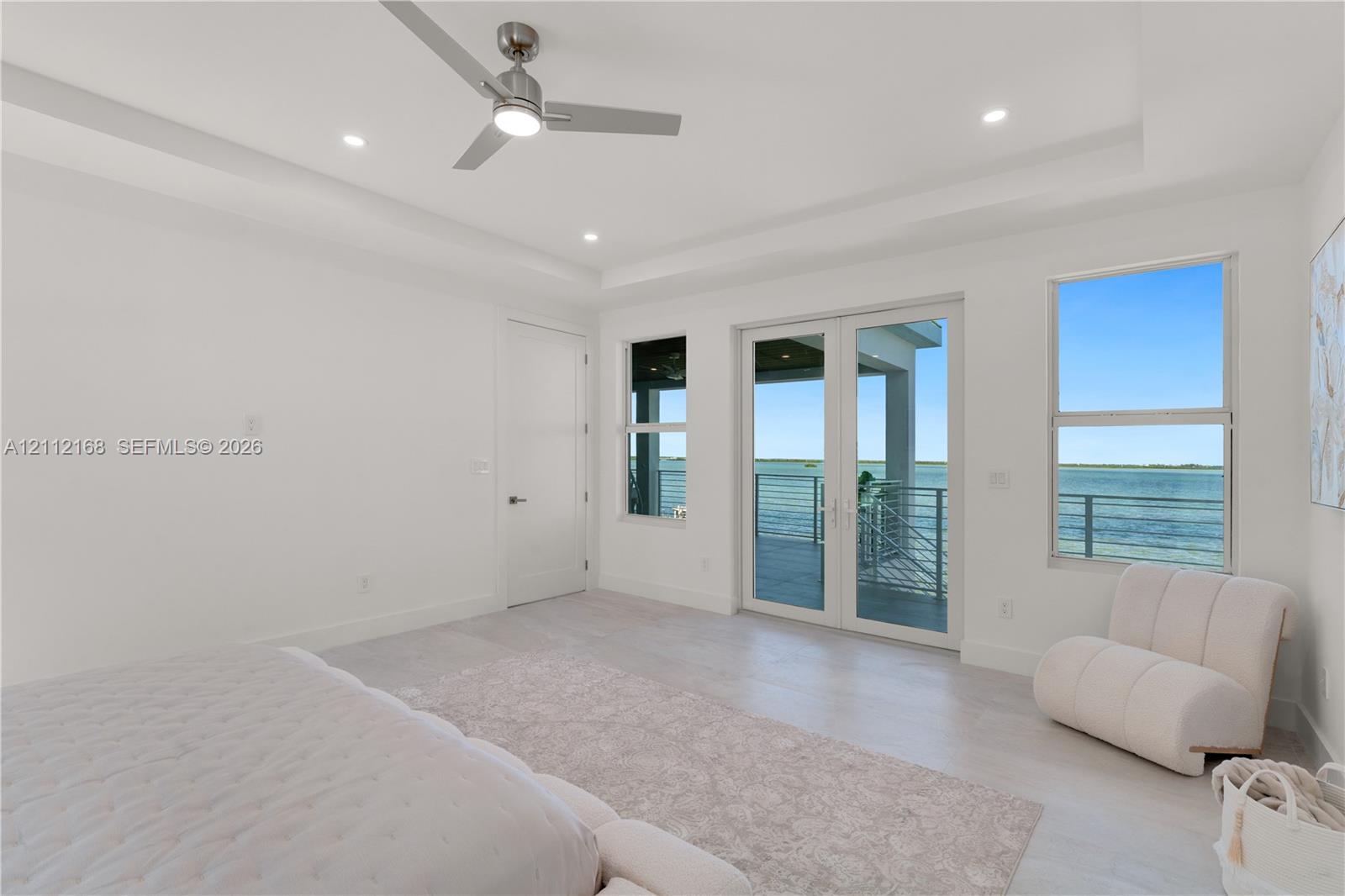 Tray ceiling with brushed nickel ceiling fan, wood-finish flooring, double-glass French doors, and waterfront exterior balcony