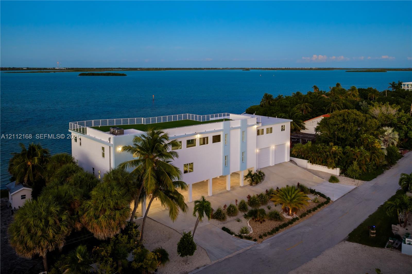 Multi-story waterfront residence featuring a rooftop terrace, elevated construction, multi-car garage, and established landscaping