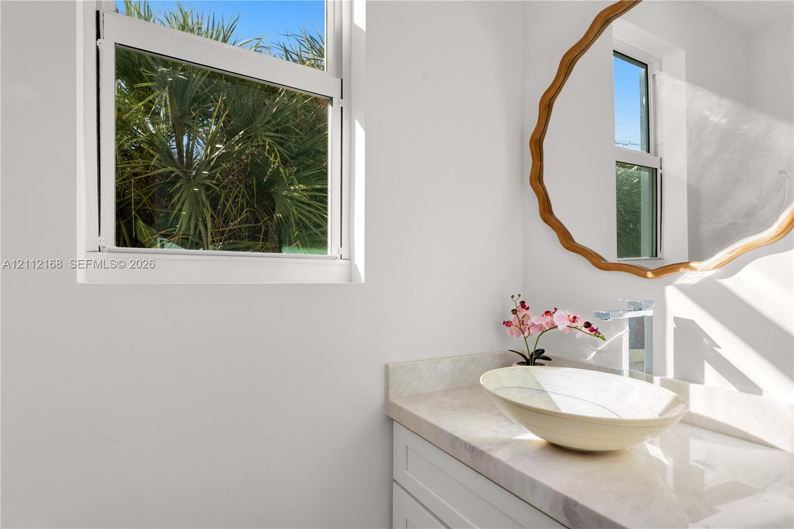 Vanity featuring a stone-surface countertop, an oval vessel sink, a chrome single-handle faucet, and white shaker-style cabinetry, complemented by a single-hung window