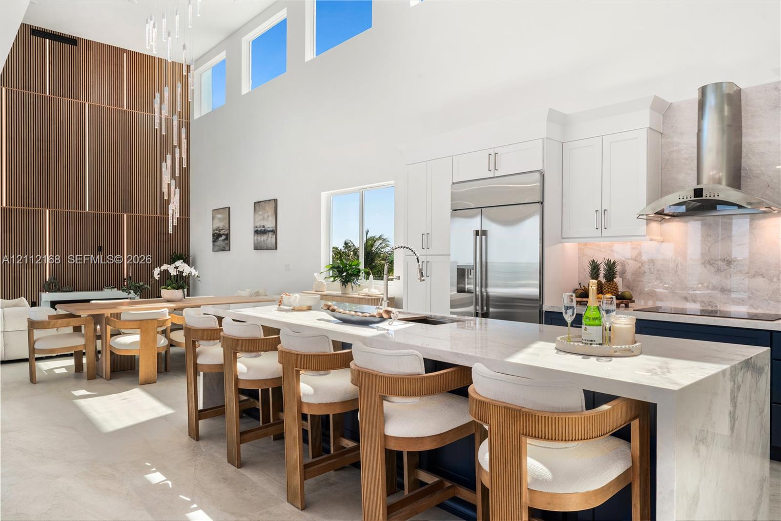 Kitchen featuring a waterfall island with stone countertop, cabinetry with integrated appliances, vertical wood-paneling wall feature, soaring ceilings with transom windows, and a multi-pendant light fixture