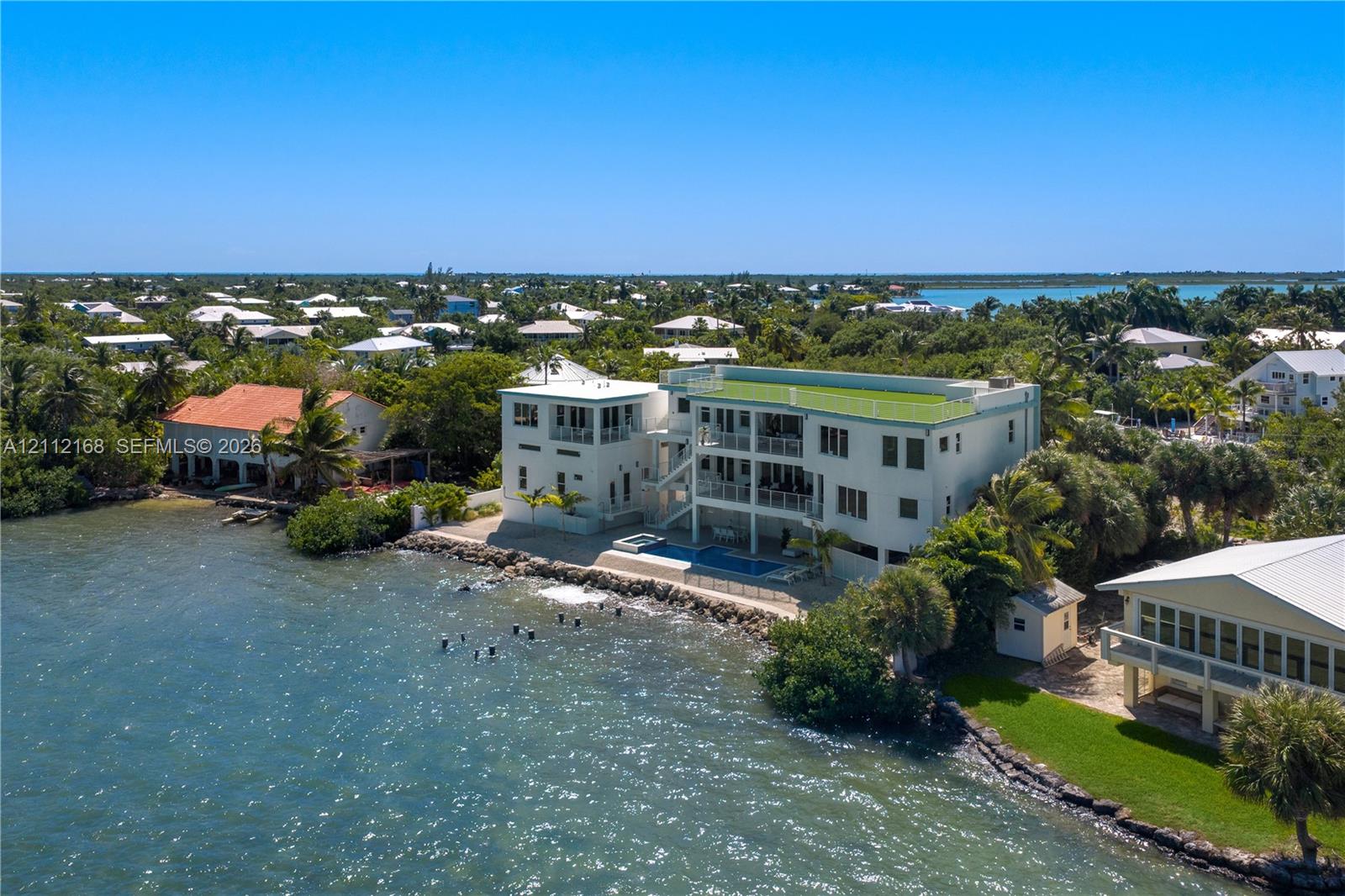 Waterfront multi-story residence featuring a private pool, multiple tiered balconies, a rooftop terrace, and stone shoreline stabilization