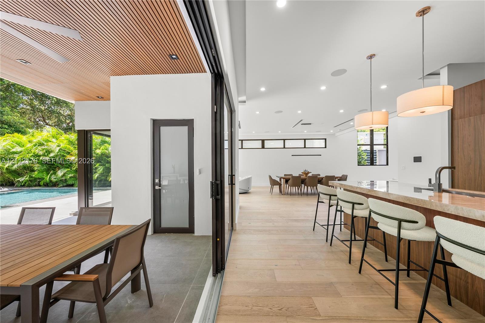 Covered patio featuring a slatted wood ceiling and recessed lighting, retractable multi-panel glass doors, wide-plank wood-finish flooring, kitchen island with stone countertop, and pendant lighting