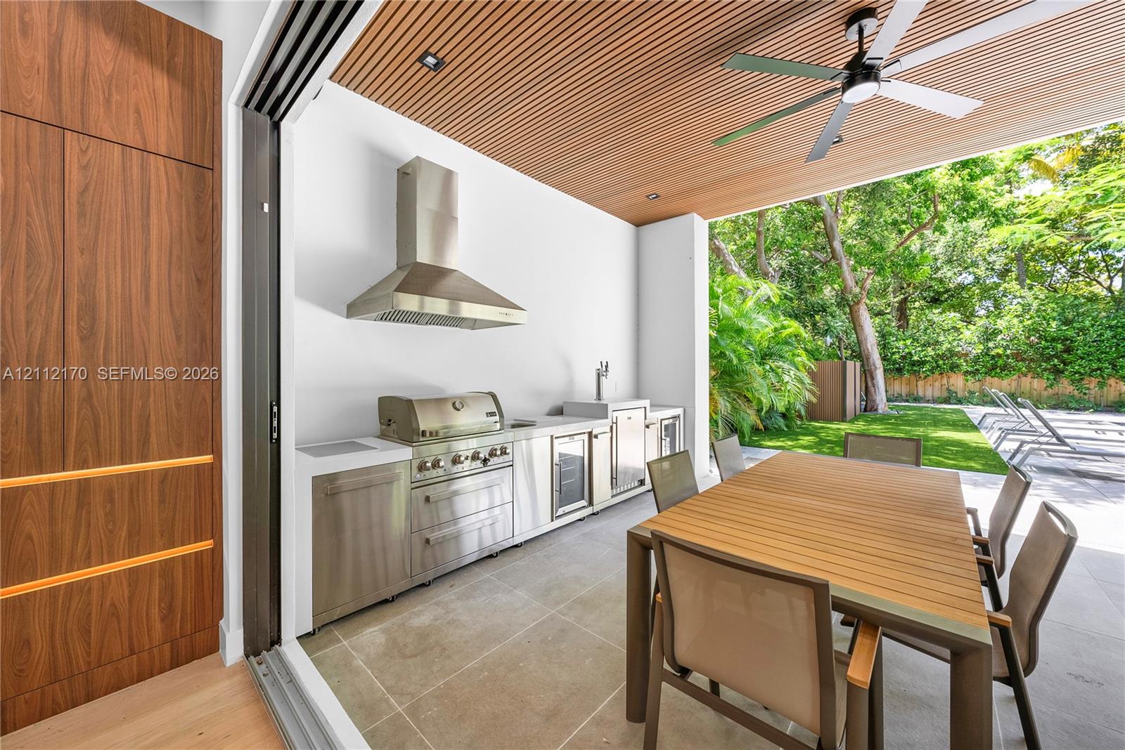 Covered outdoor kitchen featuring stainless steel appliances, quartz countertops, a linear wood-slat ceiling, and a ceiling-mounted fan