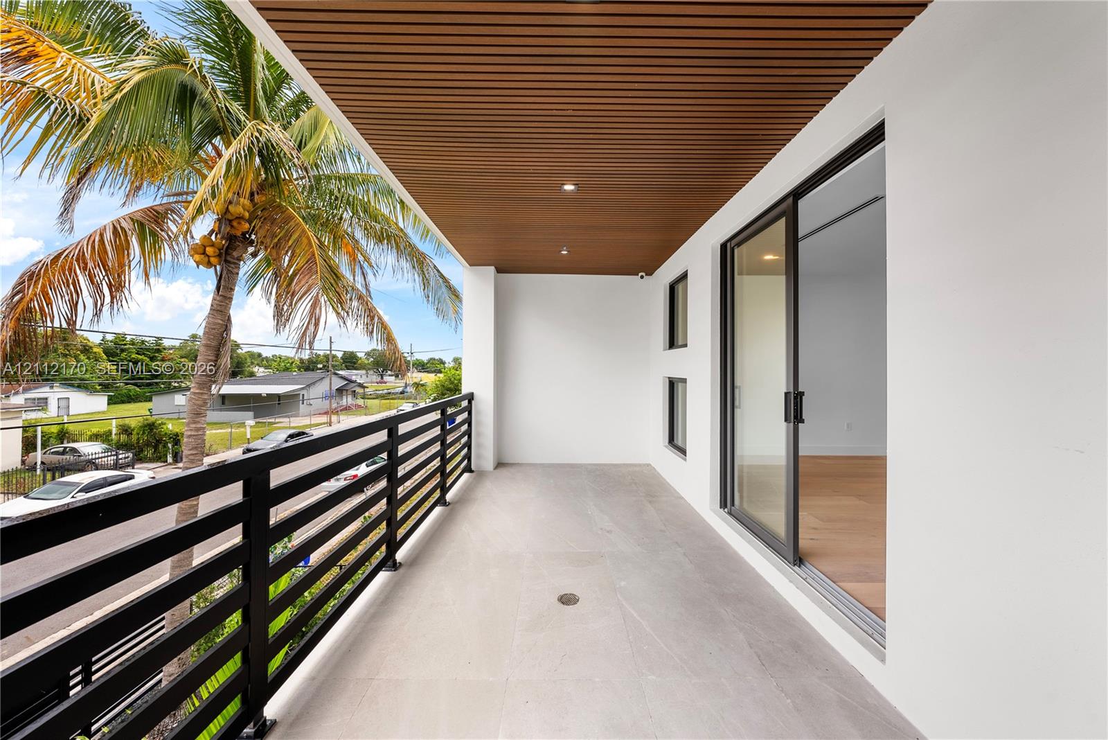 Covered balcony featuring a slatted wood-finish ceiling, recessed lighting, large-format tile flooring, and a black horizontal metal railing