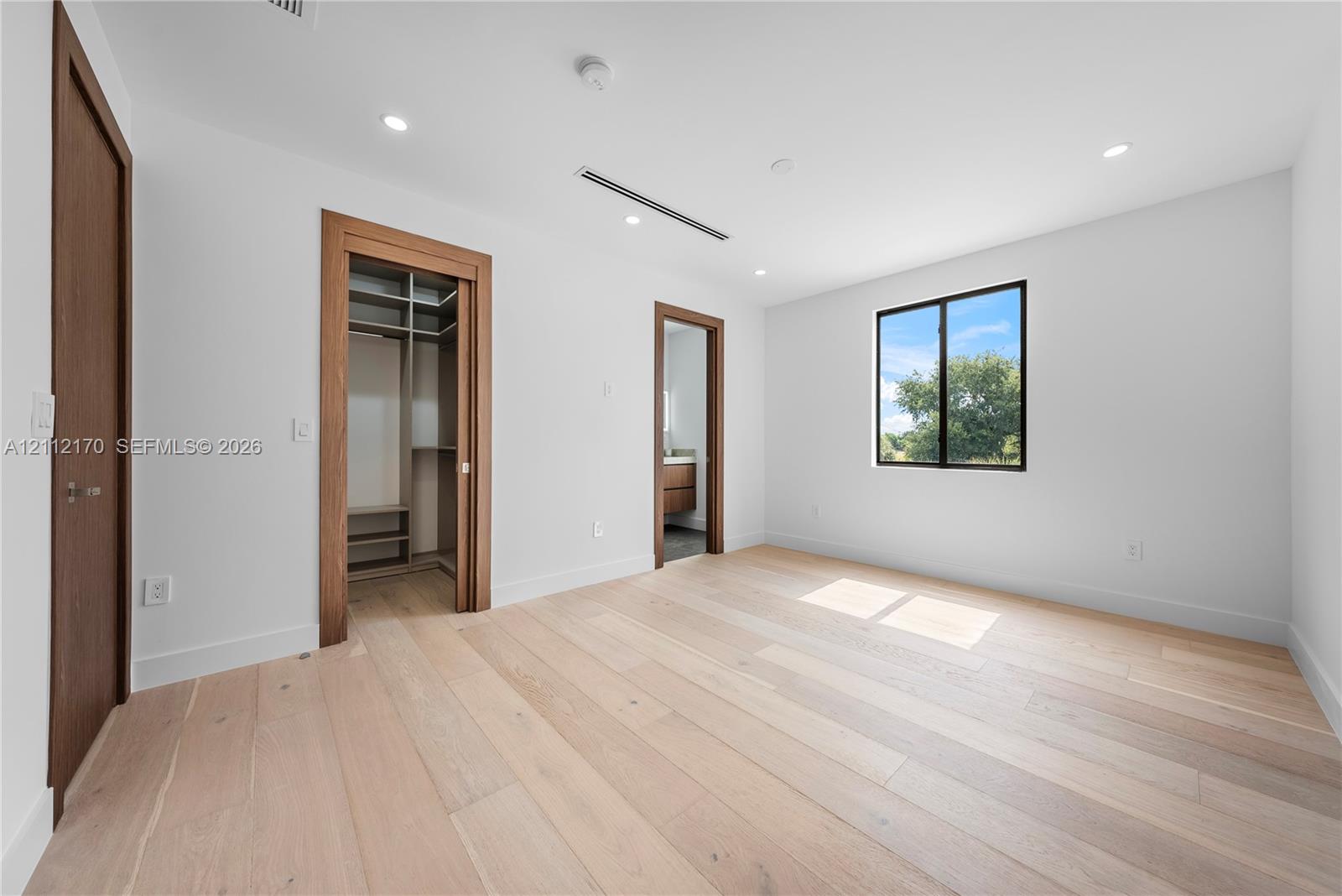 Room featuring wood-finish flooring, recessed lighting, wood-trimmed door frames, and a walk-in closet with built-in shelving