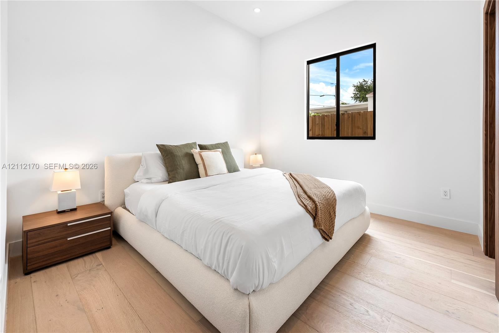 Bright room featuring light wood-finish flooring, a single window with a black frame, and recessed lighting