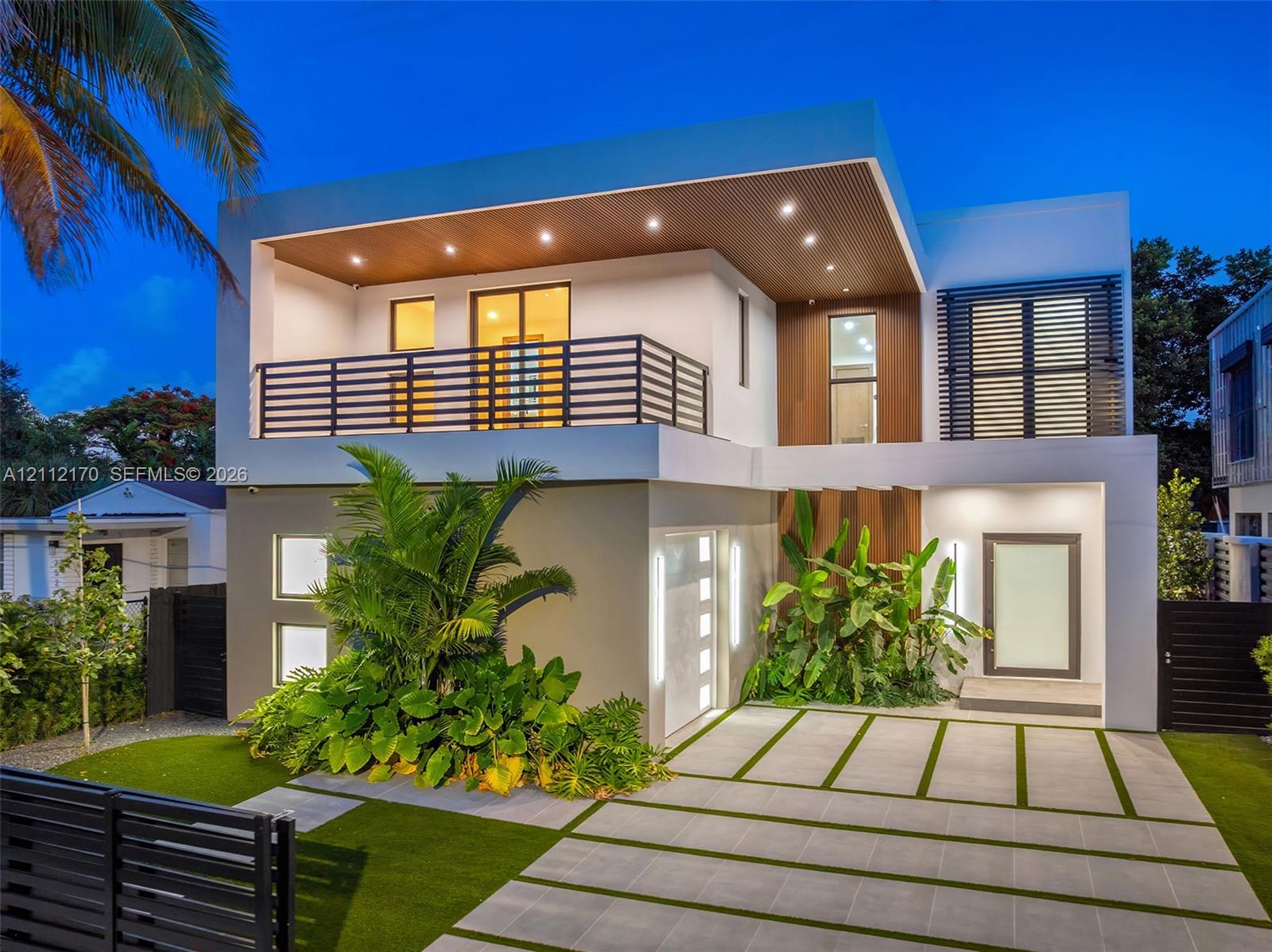 Contemporary two-story exterior featuring smooth stucco siding, wood-finish soffit detailing, a second-level balcony with horizontal slat railings, and an integrated paver driveway