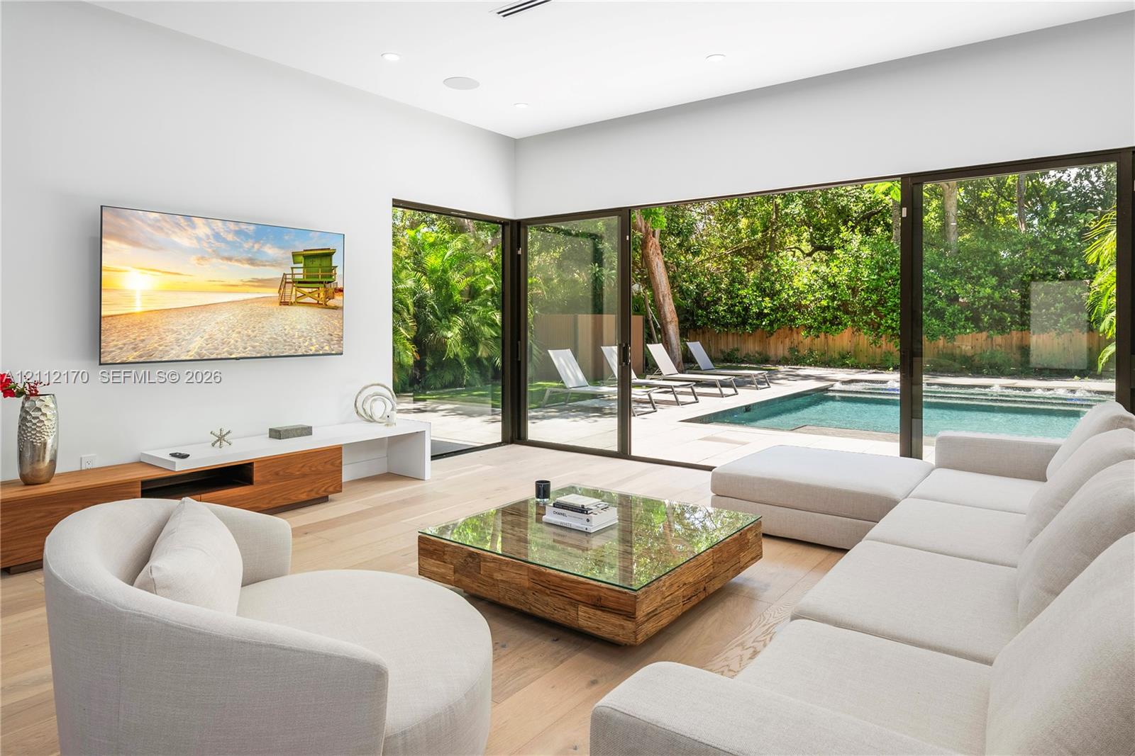 Living area featuring wood-finish flooring, recessed lighting, and wall-to-wall sliding glass doors, opening to an exterior patio and swimming pool
