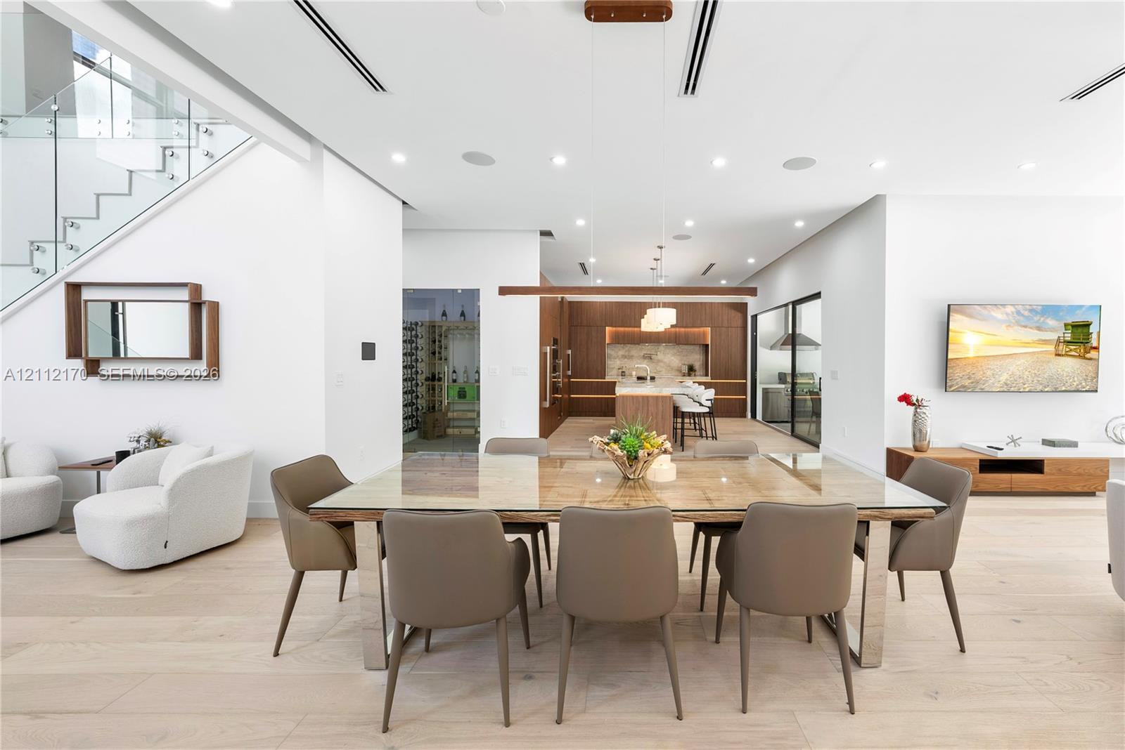 Open-concept interior featuring light wood-finish flooring, glass-railing staircase, linear recessed lighting, built-in temperature-controlled wine storage, and custom cabinetry