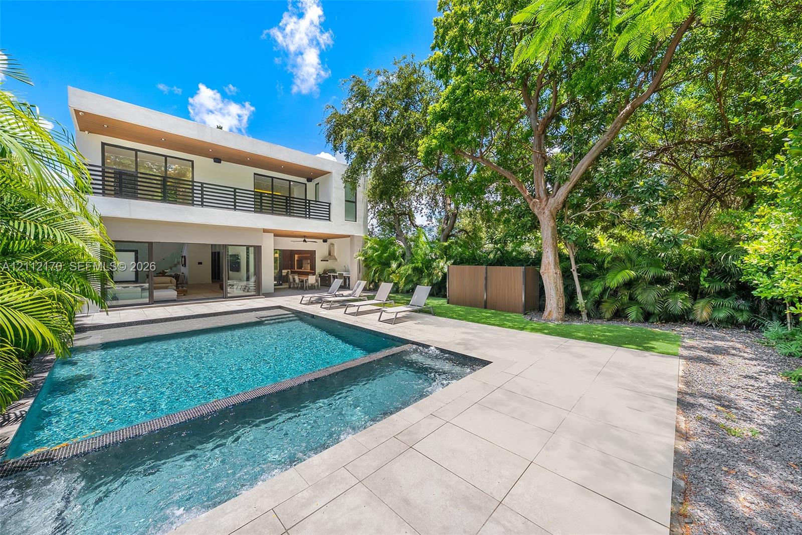 Modern two-story residence featuring an in-ground swimming pool with an integrated spa, large format tile patio, balcony with horizontal railings, and expansive sliding glass doors