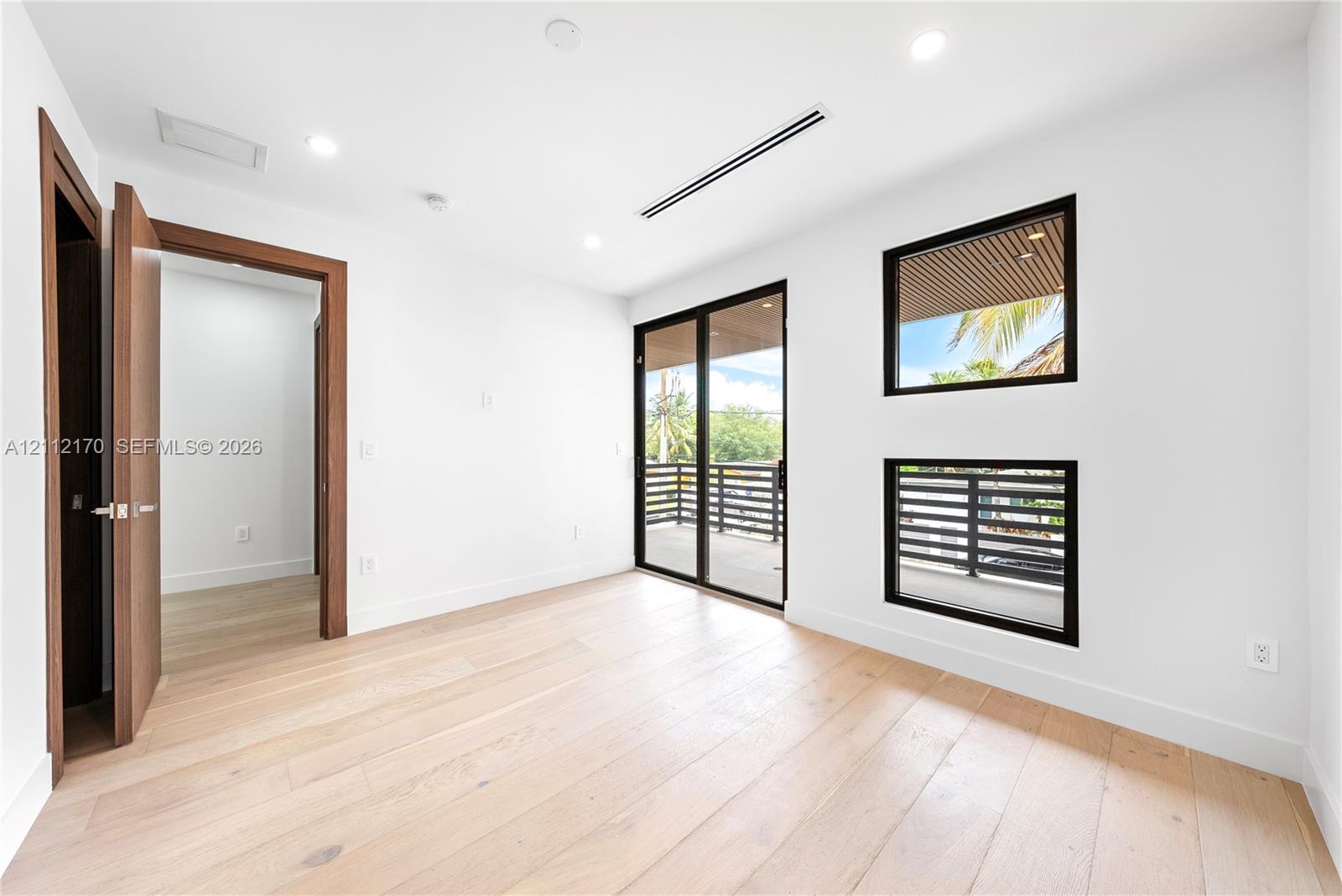 Room featuring light wood-finish flooring, recessed lighting, floor-to-ceiling glass sliding doors, dual rectangular windows with black frames, and solid wood-finish door casing