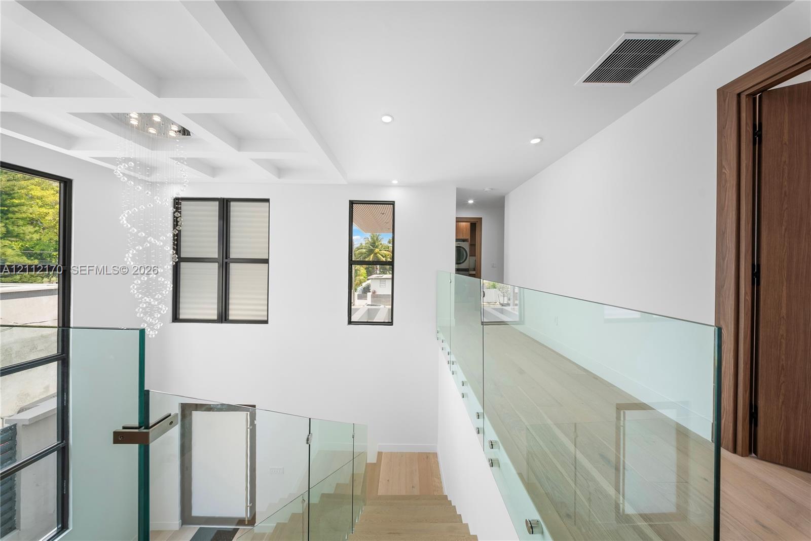 Coffered ceilings, frameless glass panel railings, wood-finish flooring, and multi-pane windows with black frames