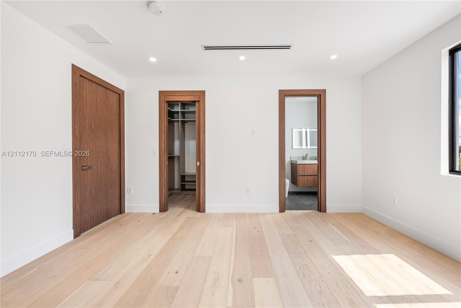 Light wood-finish flooring, recessed lighting, wood-trim door frames, built-in closet shelving, and a floating vanity