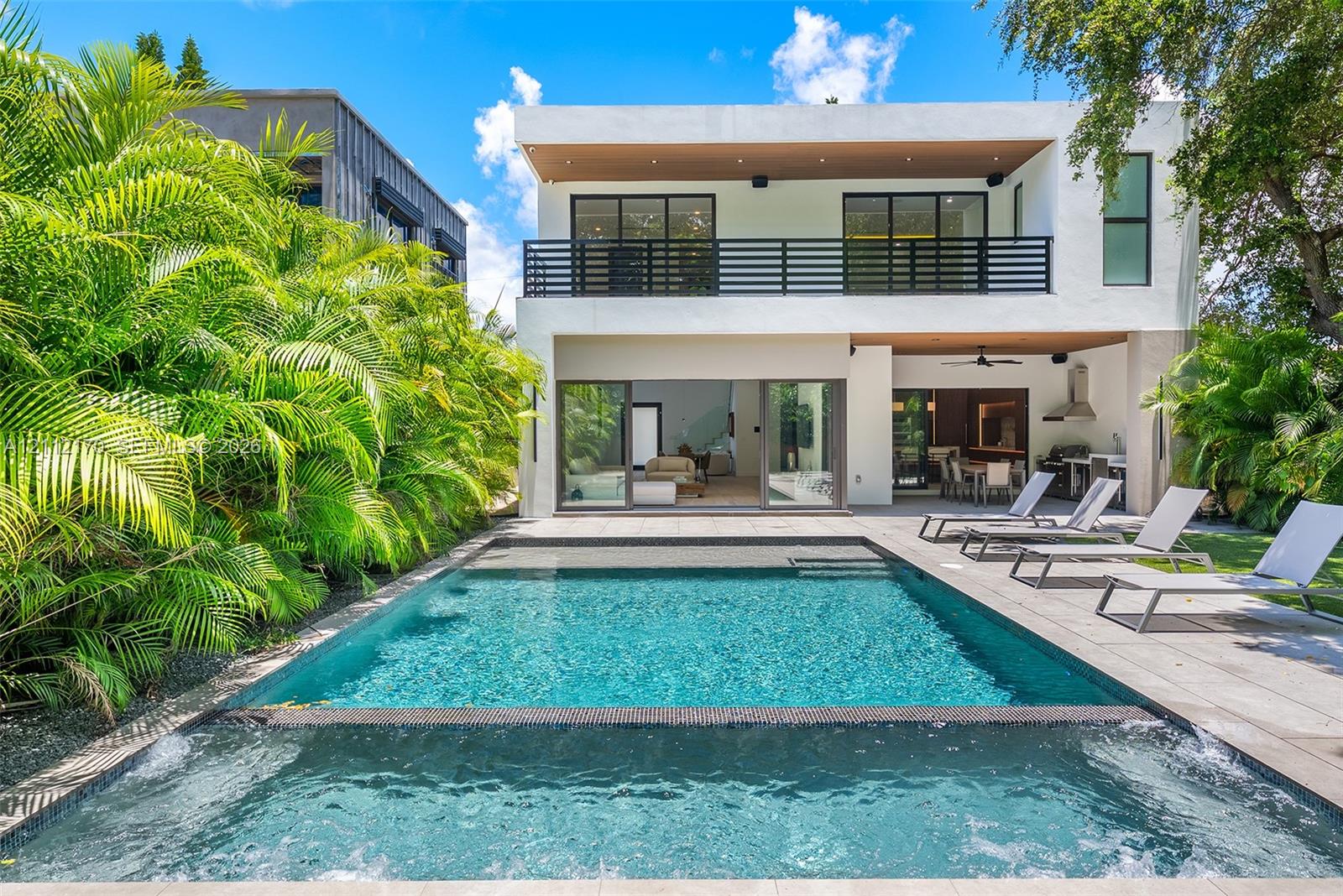 Modern exterior featuring a swimming pool with integrated spa, concrete patio, second-story balcony with horizontal railing, and sliding glass doors