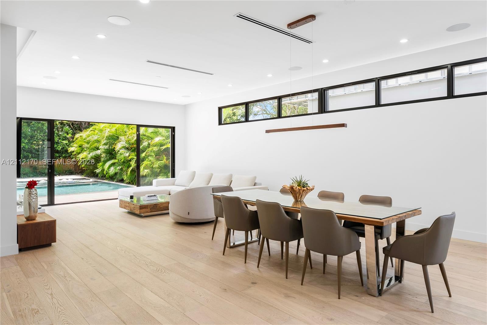 Open-concept interior featuring light wood-finish flooring, recessed lighting, clerestory windows, and large-format sliding glass doors with black frames