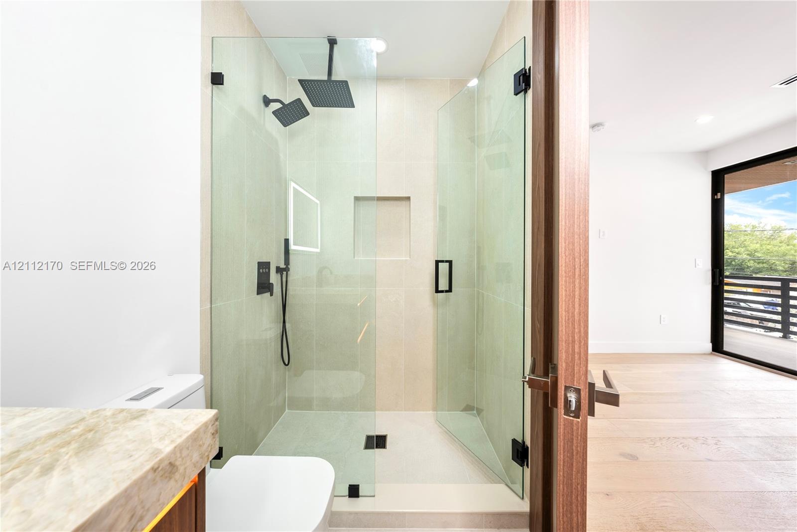 Walk-in shower featuring a glass enclosure, dual rainfall showerheads, matte black fixtures, and a recessed wall niche, paired with stone-finish countertop cabinetry and light-toned wood-finish flooring