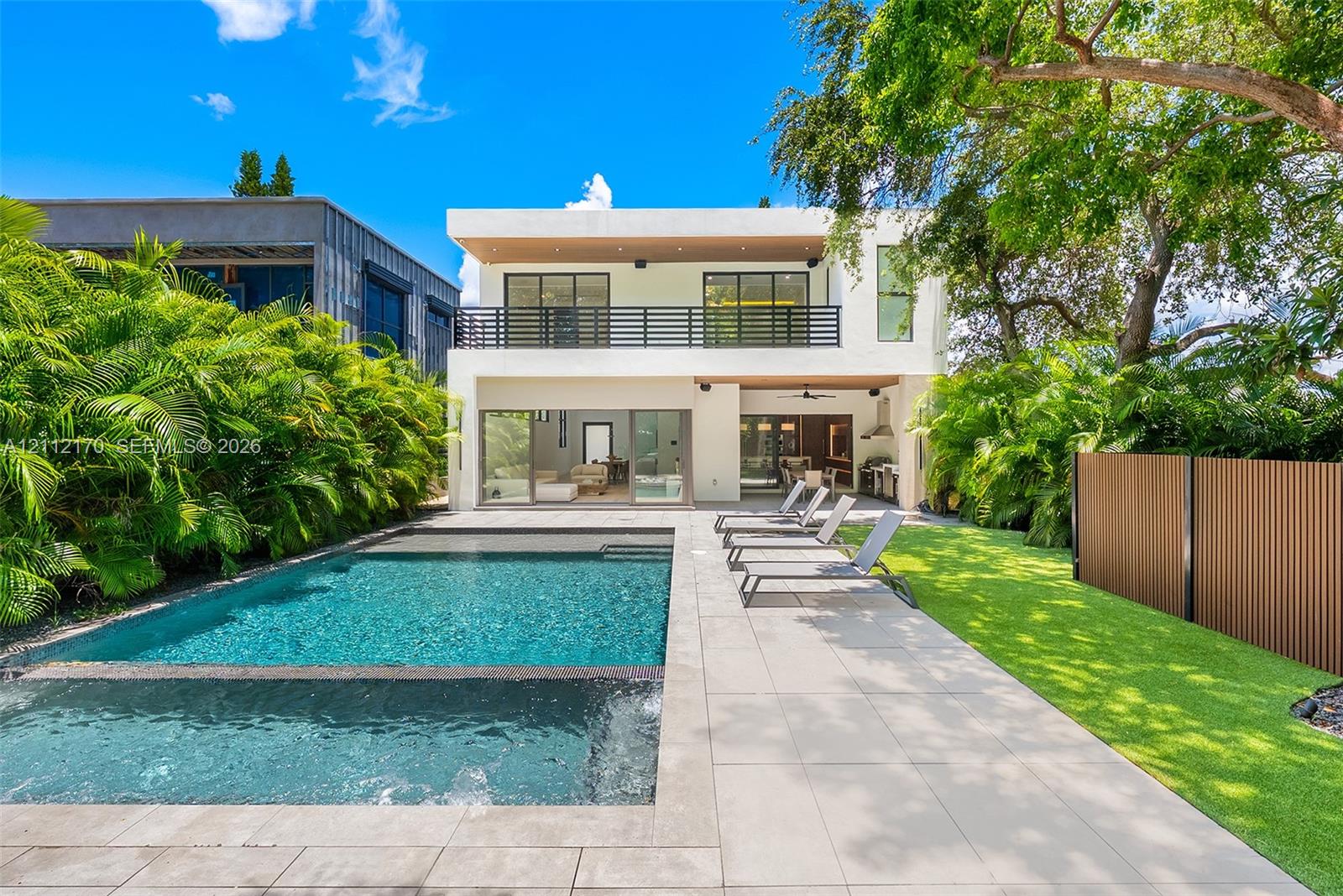 Modern two-story residence featuring a pool with integrated spa, large-format tile patio, second-story balcony with metal railing, and built-in outdoor kitchen