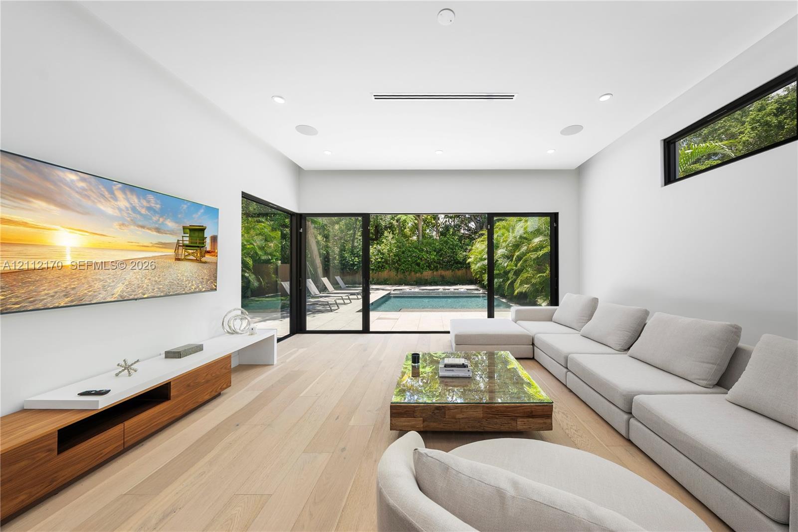 Wood-finish flooring, floor-to-ceiling sliding glass doors, built-in cantilevered media console, recessed ceiling lighting, and clerestory window