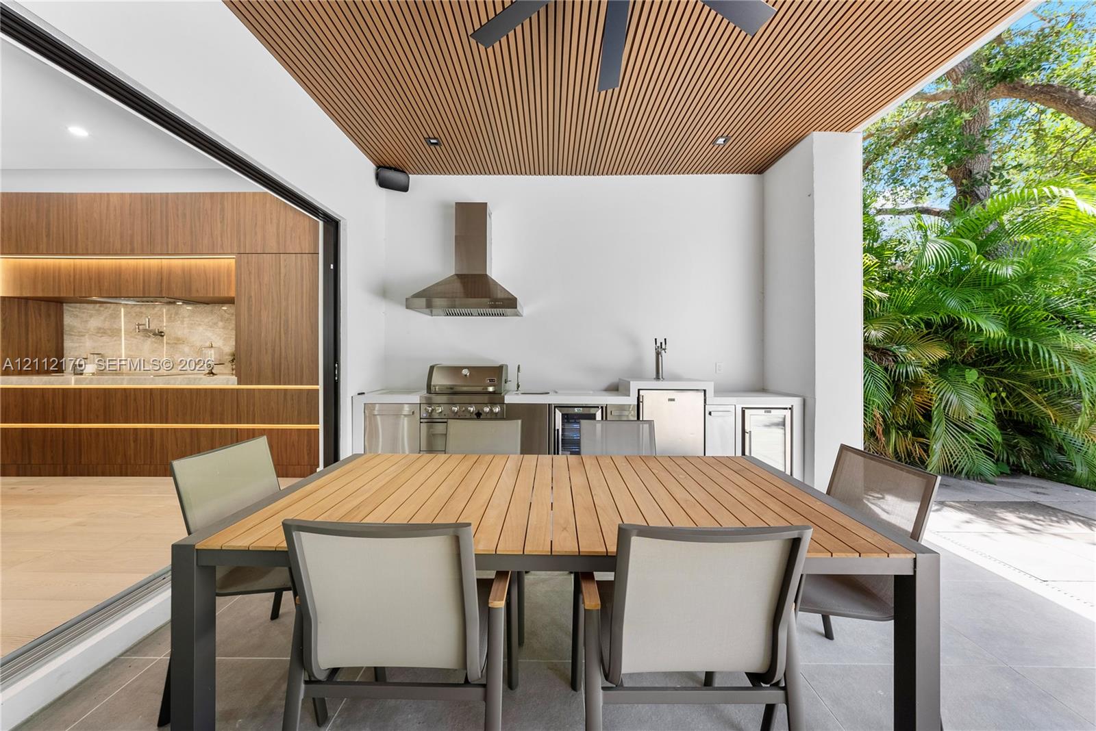 Covered outdoor kitchen featuring a stainless steel grill, beverage cooler, sink, and linear wood-slat ceiling finish