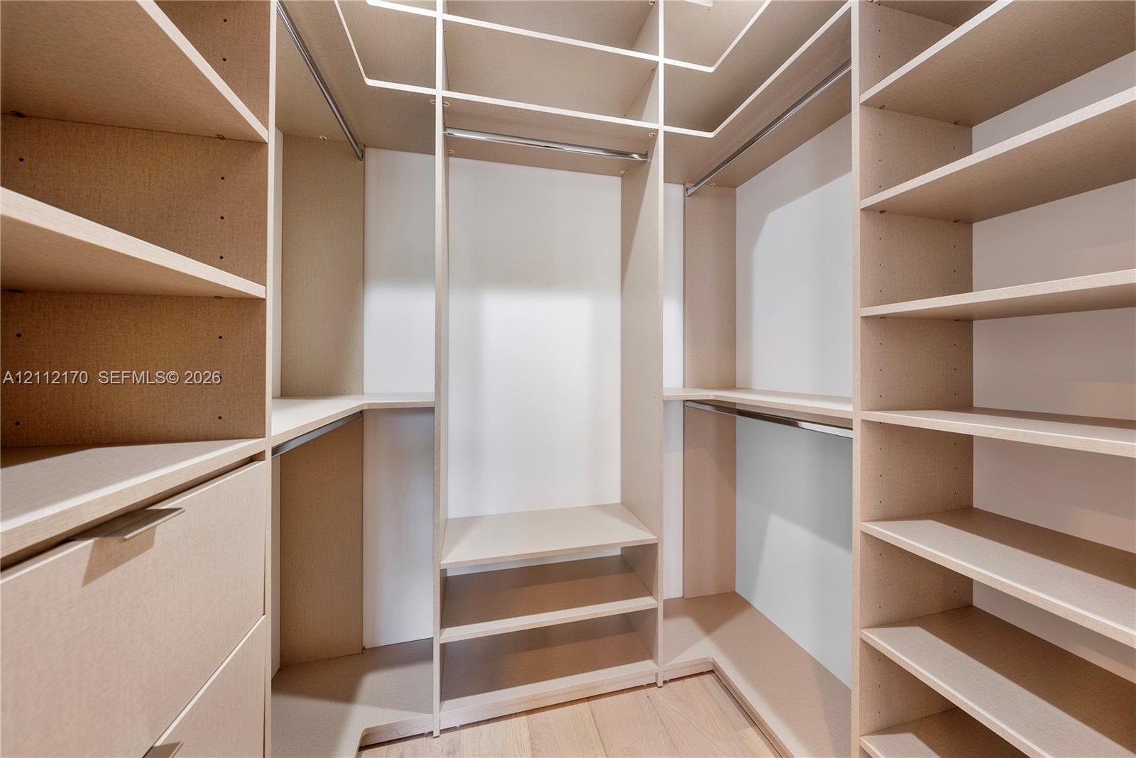 Walk-in closet featuring floor-to-ceiling built-in cabinetry, custom shelving, integrated hanging rods, and wood-finish flooring