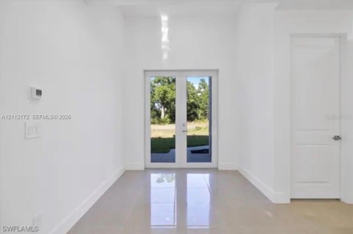 Interior space featuring high ceilings, polished tile flooring, double-panel glass entry doors, and a solid-core interior door Interior space featuring high ceilings, polished tile flooring, double-panel glass entry doors, and a solid-core interior door