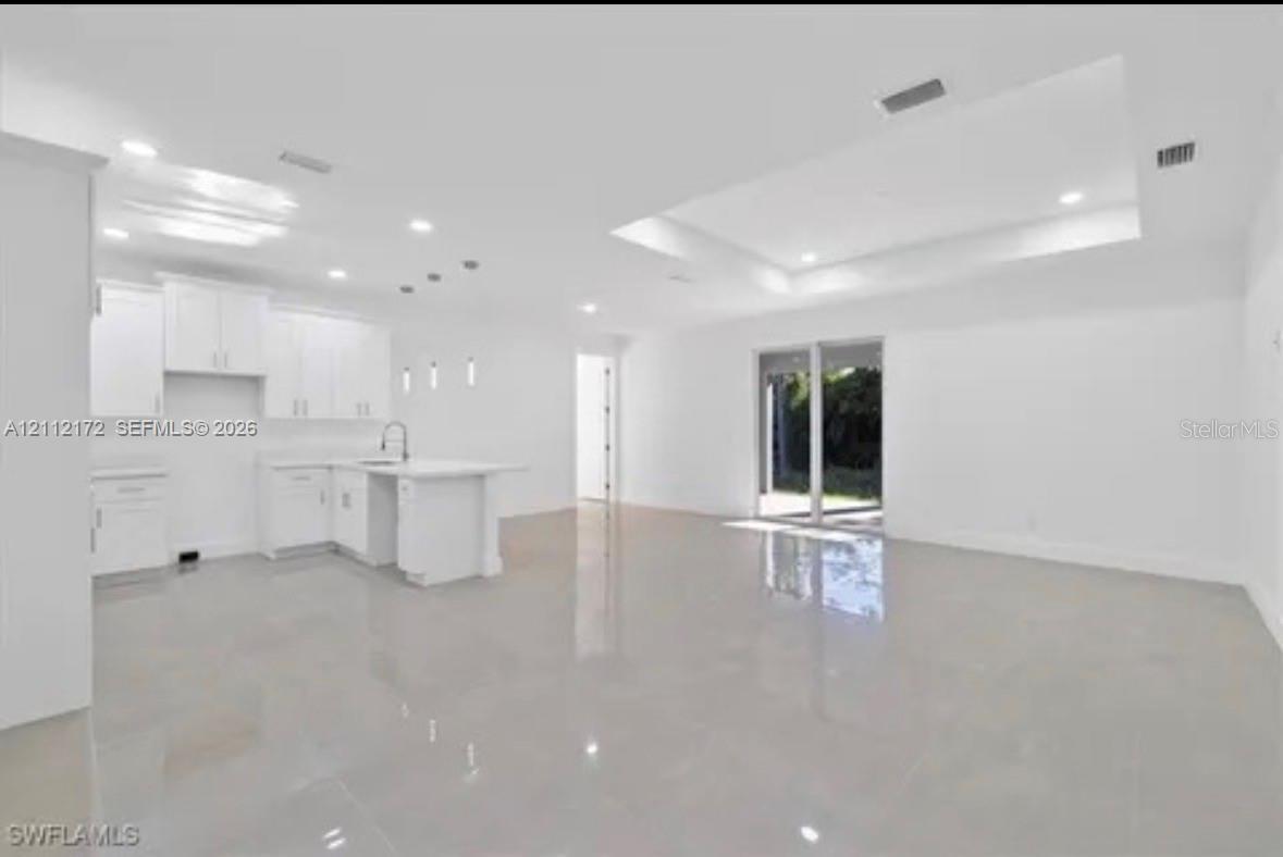 Open-concept floor plan featuring recessed lighting, a coffered ceiling, polished tile flooring, and a kitchen with white cabinetry and a center island Open-concept floor plan featuring recessed lighting, a coffered ceiling, polished tile flooring, and a kitchen with white cabinetry and a center island