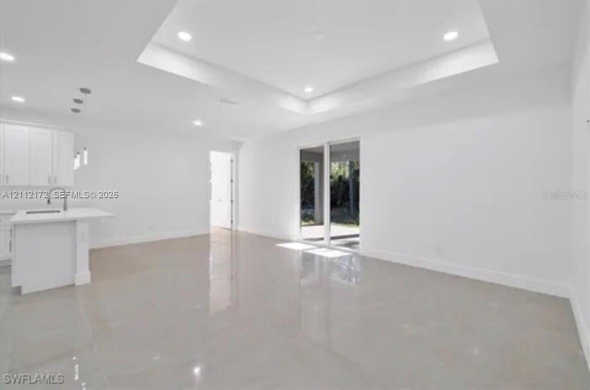 Open-concept interior featuring a tray ceiling, recessed lighting, polished large-format tile flooring, a kitchen island with stone-surface countertop, and sliding glass doors Open-concept interior featuring a tray ceiling, recessed lighting, polished large-format tile flooring, a kitchen island with stone-surface countertop, and sliding glass doors