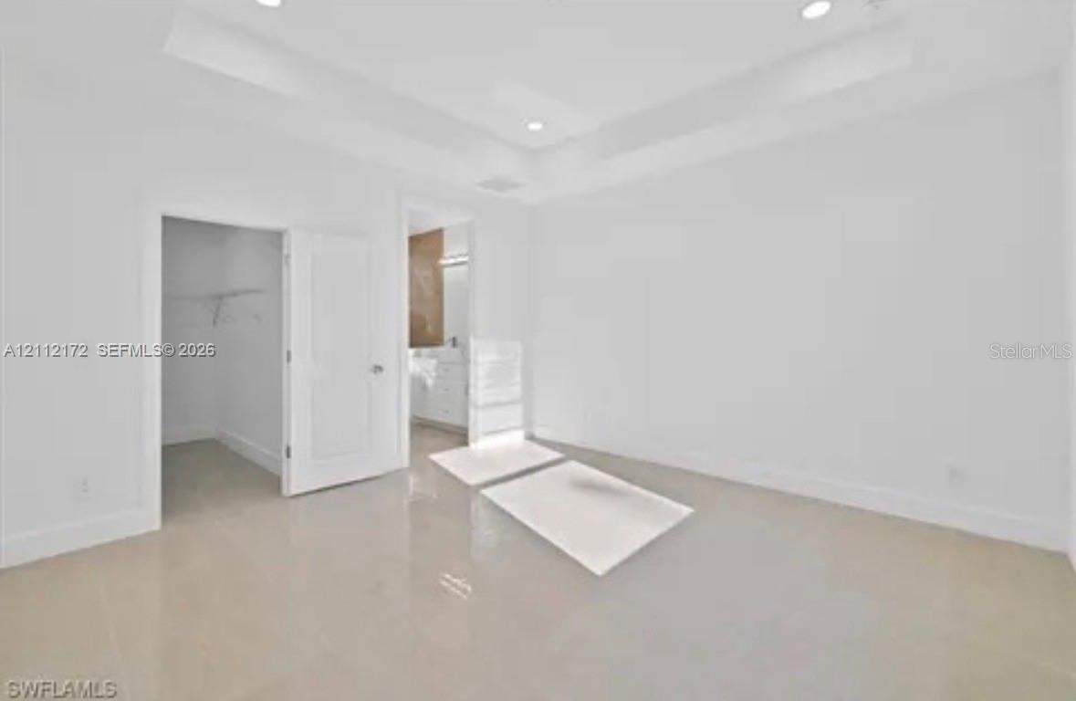 Tray ceiling with recessed lighting, large-format tile flooring, and walk-in closet featuring built-in wire shelving