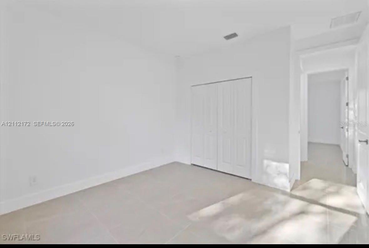 Neutral interior space featuring polished tile flooring, smooth white walls, and a built-in closet with dual paneled doors