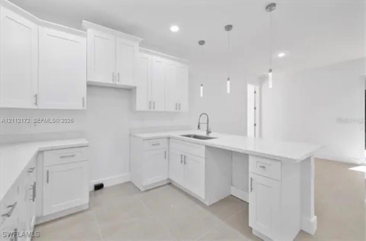 Kitchen featuring white shaker-style cabinetry, solid-surface countertops, a stainless steel undermount sink with a gooseneck faucet, three pendant lights, and light-toned tile flooring