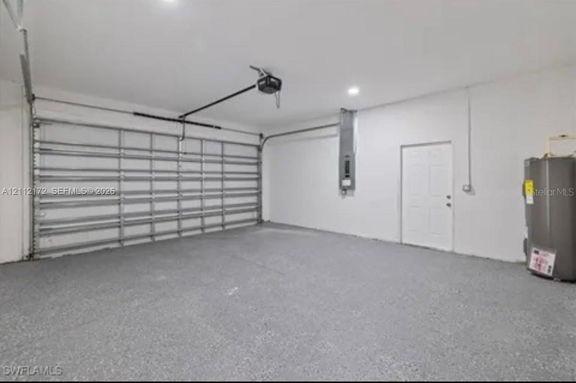Garage interior featuring a motorized sectional door, painted walls, speckled epoxy flooring, recessed lighting, and a single-panel interior access door
