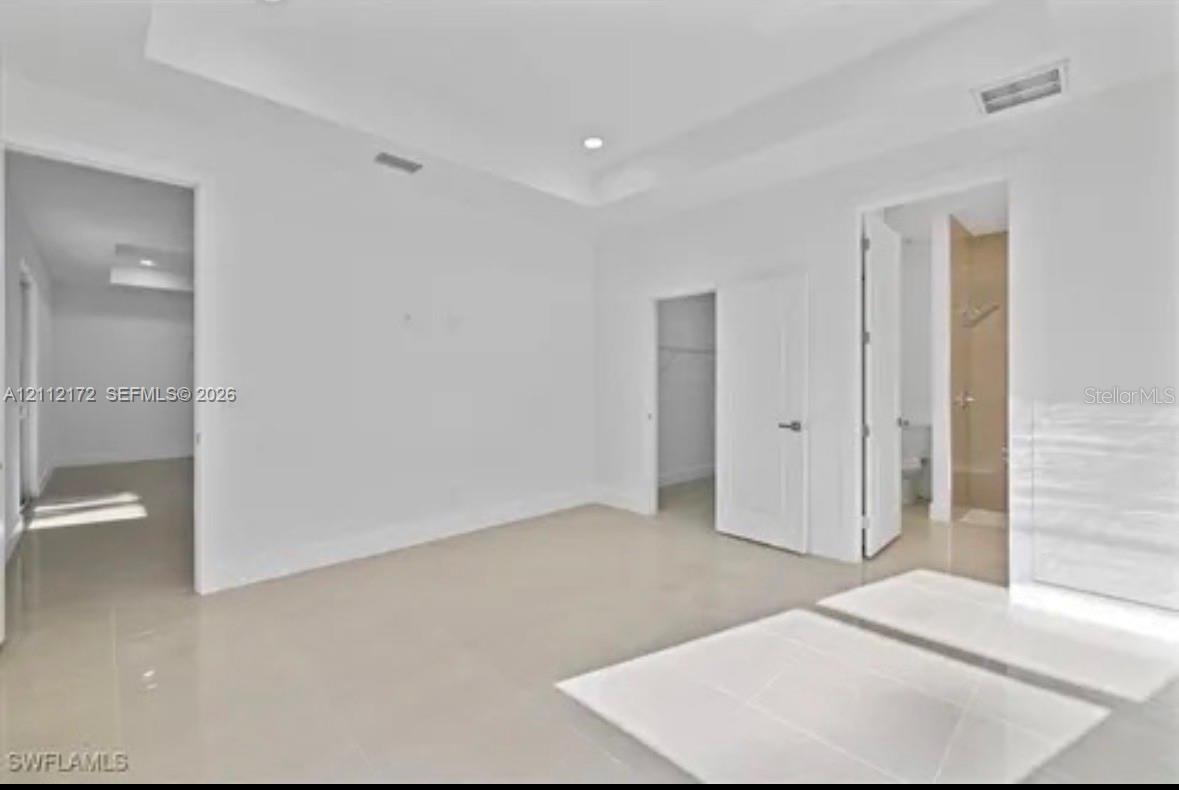 Interior space featuring neutral tile flooring, a recessed tray ceiling, recessed lighting, and solid-core interior doors