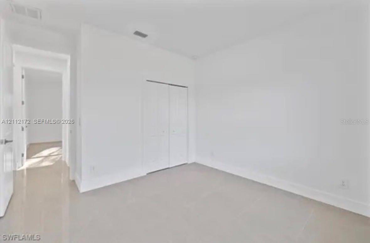 Neutral-toned interior space featuring large-format tile flooring, crisp white walls, and a built-in double-door closet