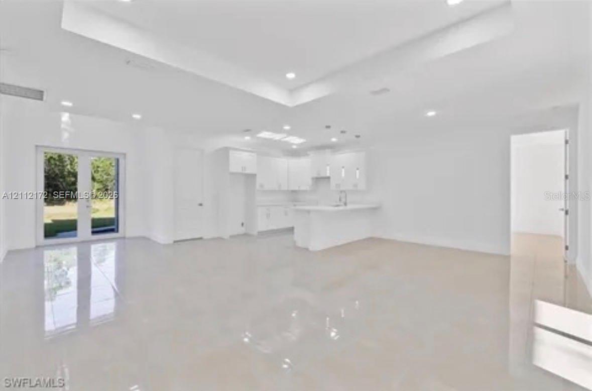 Open-concept living space featuring high tray ceilings, recessed lighting, polished tile flooring, white cabinetry, and double French doors Open-concept living space featuring high tray ceilings, recessed lighting, polished tile flooring, white cabinetry, and double French doors