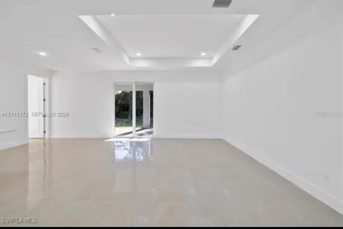 Spacious interior featuring a recessed tray ceiling, polished tile flooring, recessed lighting, and multi-panel sliding glass doors Spacious interior featuring a recessed tray ceiling, polished tile flooring, recessed lighting, and multi-panel sliding glass doors