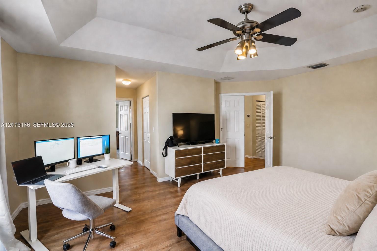 Tray ceiling featuring a central multi-blade ceiling fan with integrated lighting, wood-finish flooring, and multiple sets of interior paneled doors