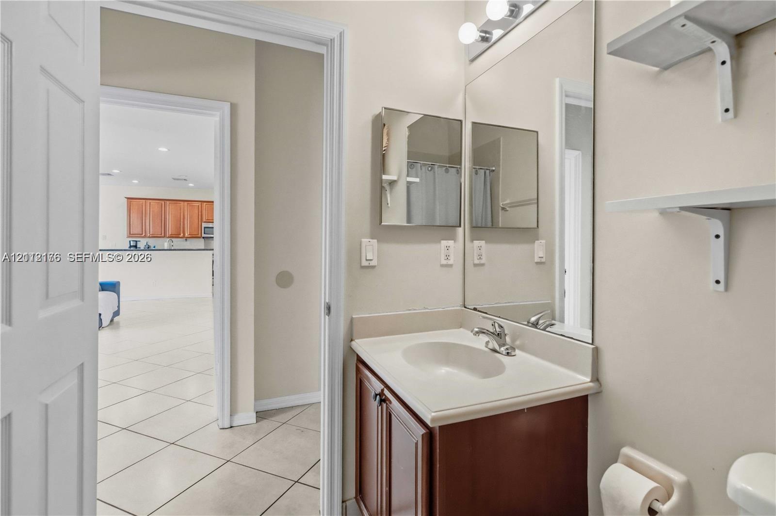 Bathroom featuring a dark wood-finish vanity, integrated sink, large wall-mounted mirror, and wall-mounted shelving