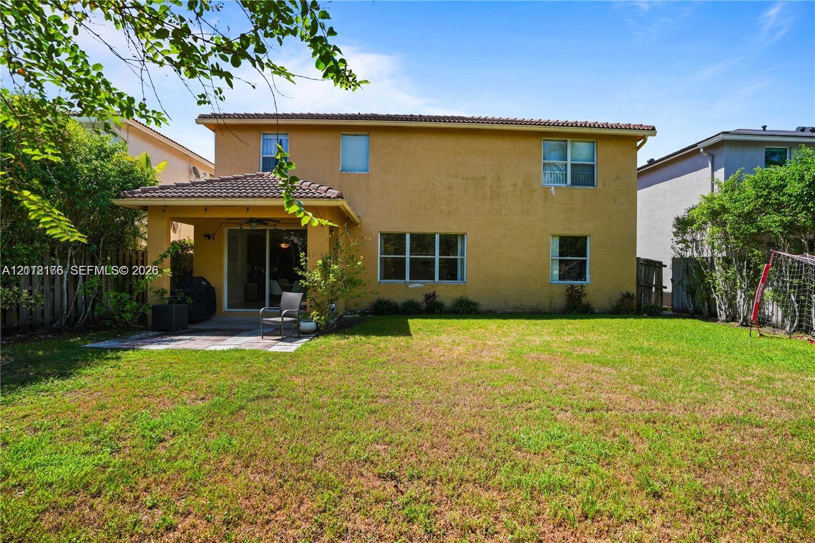 Rear exterior featuring a two-story stucco facade, a covered concrete patio, a tiled roof, and a fenced-in grassy yard