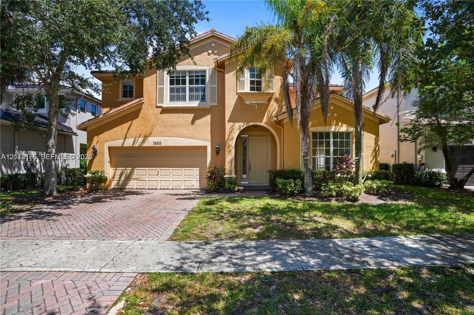 Two-story stucco exterior featuring a tiled roof, arched entryway, brick-patterned paved driveway, and decorative window shutters