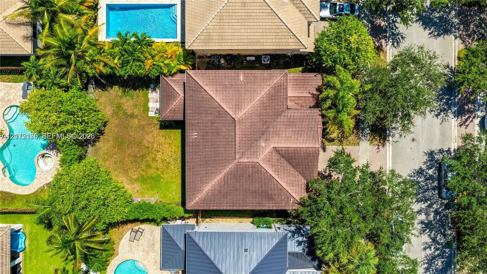 Aerial perspective featuring a hip roof structure, paved driveway, landscaped grounds with mature trees, and a swimming pool