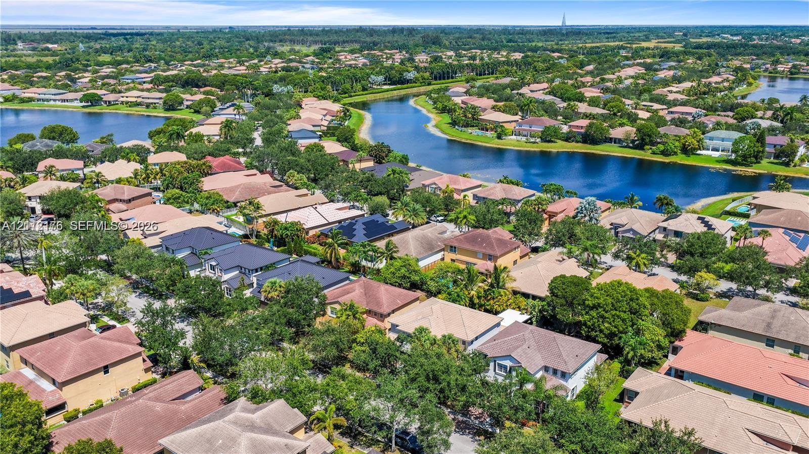 Aerial perspective of a residential neighborhood featuring multi-phase housing, winding waterways, mature landscaping, and solar panel installations