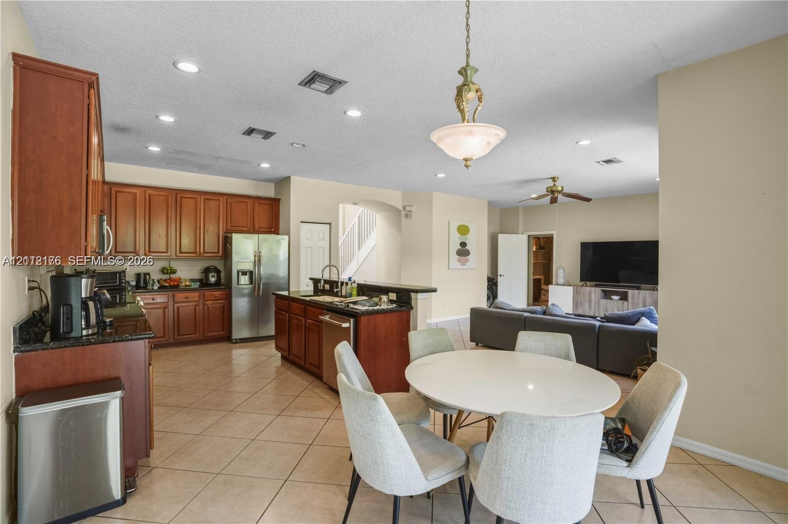 Kitchen featuring medium-tone wood cabinetry, granite countertops, a center island with integrated sink, stainless steel appliances, and tiled flooring