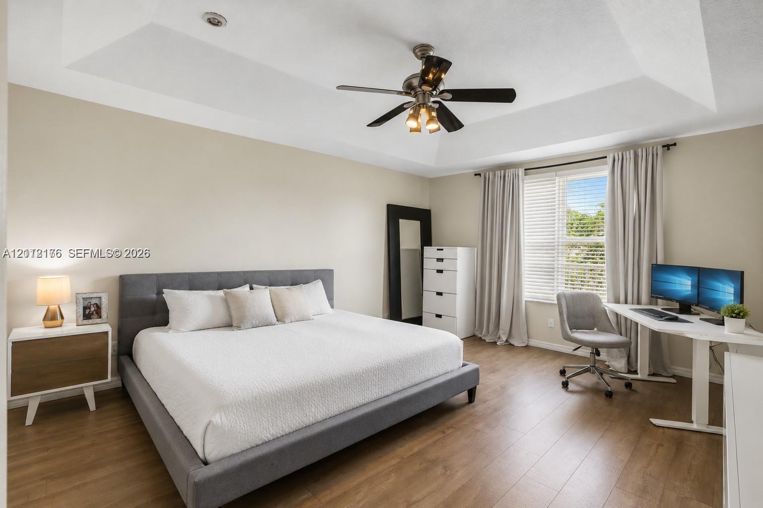 Tray ceiling featuring a central multi-light ceiling fan, wood-finish flooring, and natural light from a window with adjustable blinds
