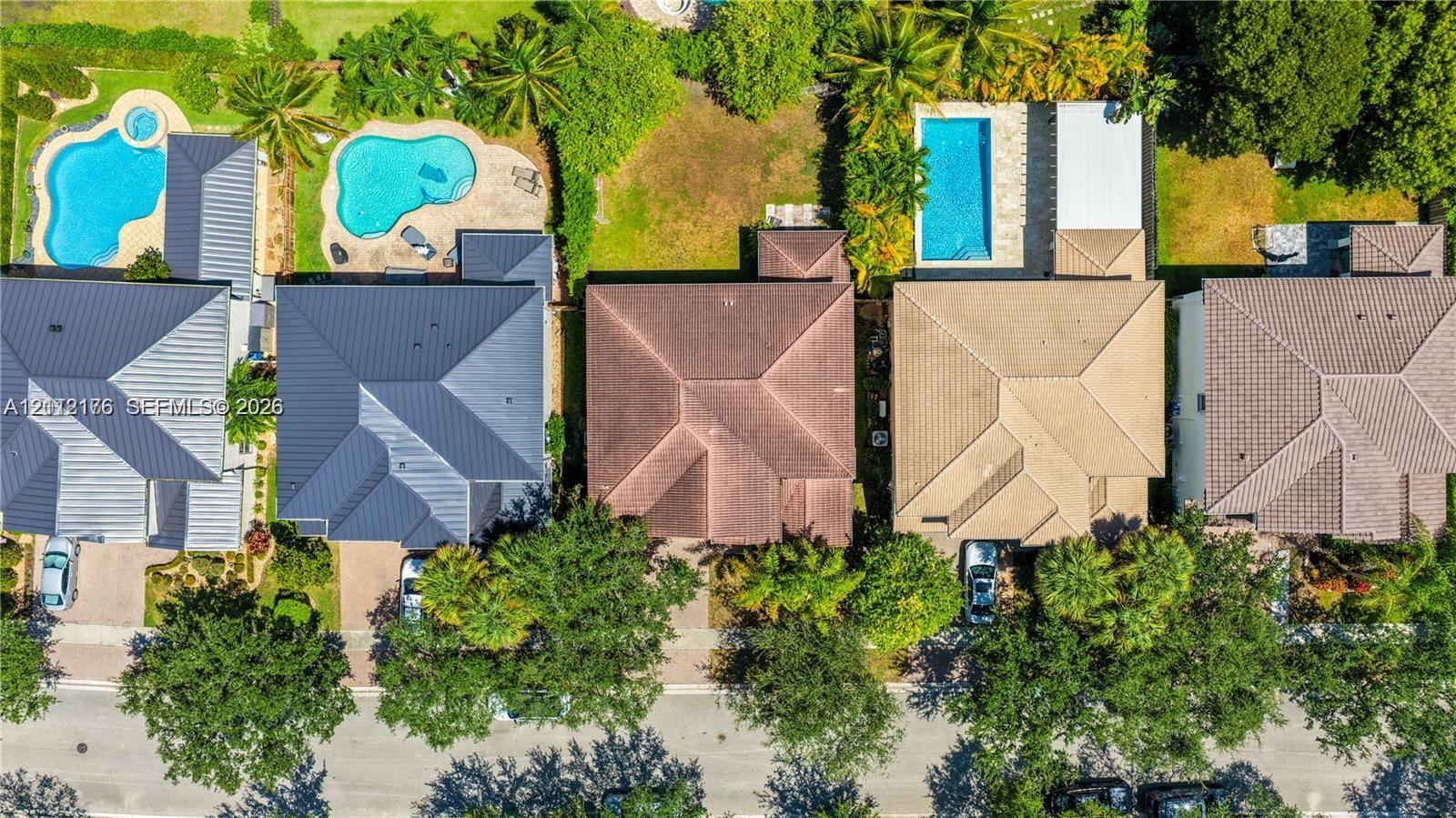 Aerial perspective of residential properties featuring hip-style roofing, paved driveways, and mature landscaping