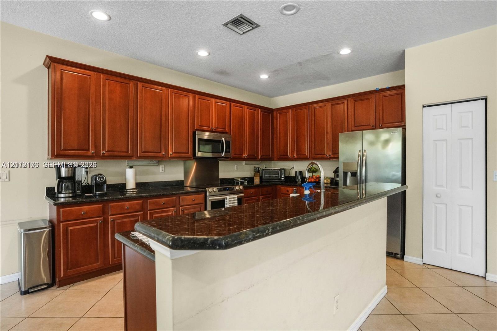 Kitchen featuring stained wood cabinetry, stone-surface countertops, breakfast bar, recessed lighting, and stainless steel appliances